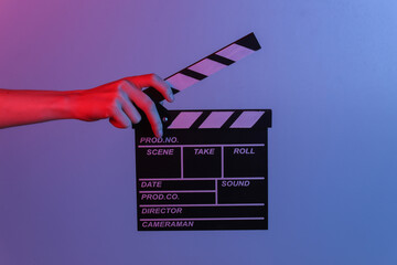 Hand holding film clapper board in blue red neon light. Cinema industry, entertainment.