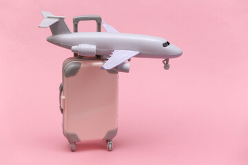 Air travel concept. Mini plastic travel suitcase, air plane on pink background.