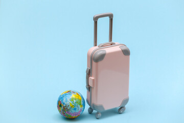 International travel concept. Mini plastic travel suitcase and globe on blue pastel  background. Minimal style