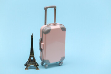 Traveled to Paris. Mini plastic travel suitcase and statuette of the Eiffel Tower on blue background.