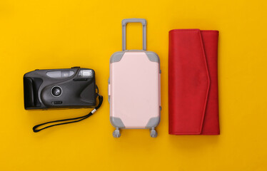 Travel flat lay. Mini plastic travel suitcase, red wallet and camera on yellow background. Minimal style. Top view