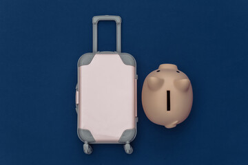 Travel flat lay. Mini plastic travel suitcase, piggy bank on classic blue background. Minimal style. Top view