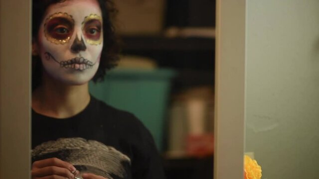 Mujer joven mexicana latina maquillaje catrina calavera d&iacute;a de muertos halloween frente al espejo tradicional festividades colorido esqueleto cara rostro blanco close-up