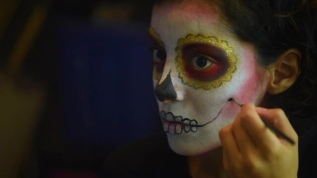 Mujer joven mexicana latina maquillaje catrina calavera d&iacute;a de muertos halloween frente al espejo tradicional festividades colorido esqueleto cara rostro blanco close-up