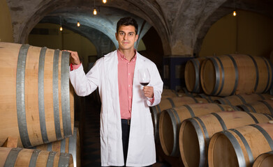 satisfied man in white robe checking ageing process of red wine. High quality photo