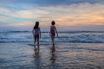 two girls entering the sea in a sunset