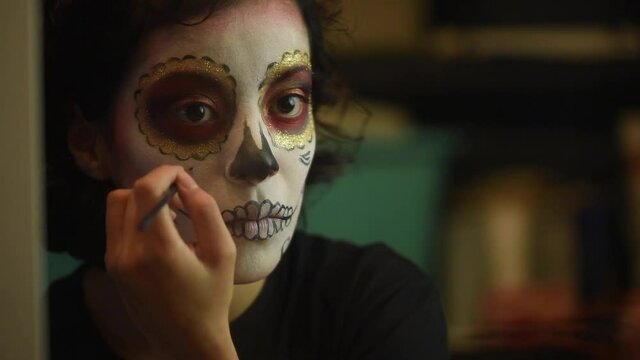Mujer joven mexicana latina maquillaje catrina calavera d&iacute;a de muertos halloween frente al espejo tradicional festividades colorido esqueleto cara rostro blanco close-up