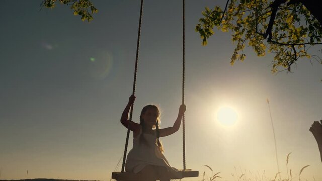 Amusement park dream concept. Happy girl swinging on a swing in the park at sunset. child plays with wooden swing, childhood dream, airplane pilot flights to the sky. A happy family