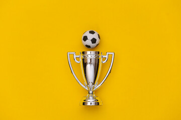 Mini soccer ball and champion cup on yellow background. Minimalism Sport concept. Top view. Flat lay