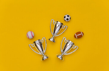 Mini different sports balls and champion cups on yellow background. Minimalism Sport concept. Top view. Flat lay.