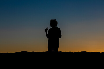 silhouette of a person standing on a hill looking in profile index fingers raised as an expression