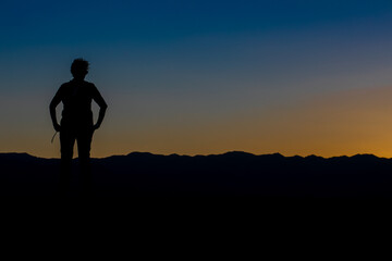 silhouette of a woman from the front with her arms on her hips in a sunset with the sky divided by yellow and blue