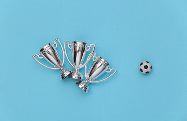 Mini soccer ball and championship cups on blue background. Minimalism Sport concept. Top view. Flat lay