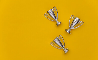 Mini silver sports championship cups on yellow pastel background. Copy space. Sport minimalism. Top view