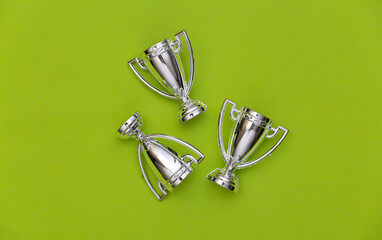 Mini silver sports championship cups on green background. Sport minimalism. Top view