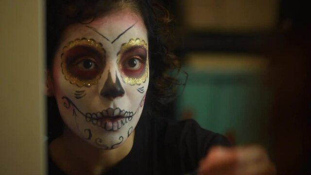 Mujer joven mexicana latina maquillaje catrina calavera d&iacute;a de muertos halloween frente al espejo tradicional festividades colorido esqueleto cara rostro blanco close-up