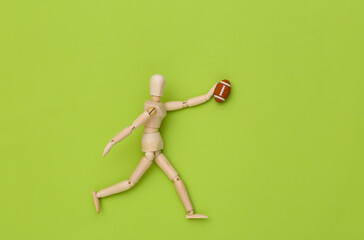 Mini wooden puppet runs with a rugby ball on a green background