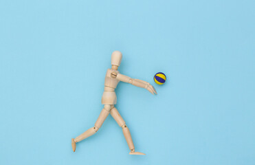 Wooden puppet plays volleyball with ball on blue background