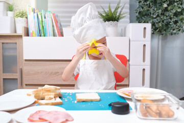 Cute Asian boy wearing chef hat and apron having fun preparing sandwiches, Little kid making cookie...