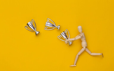 Wooden puppet holding a silver championship cups on yellow background
