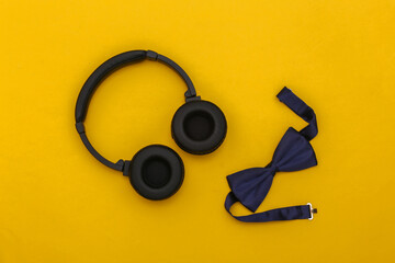 Headphones and bow tie on yellow background. Top view