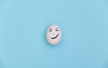 Fototapeta na wymiar Chicken egg with hand drawn happy face on a blue background.