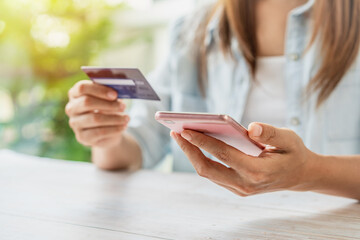 Young woman holding a credit card and using smartphone for making online payment shopping
