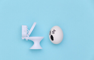 Diarrhea or poisoning. Egg face and mini toilet on a blue background