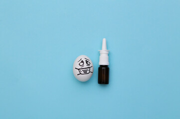 The egg face in a medical mask and nasal spray on blue background. Covid-19 pandemic. Top view