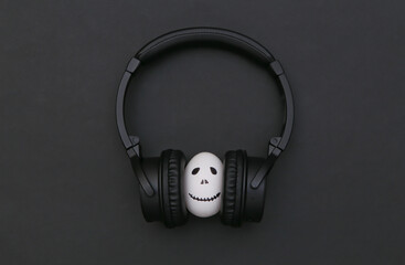 Fototapeta premium Halloween theme. Egg with hand drawn scary ghost face listen music in headphones on black background