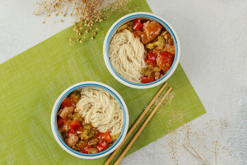 Chicken teriyaki with bell peppers, broccoli and noodles in bowl with chopsticks.