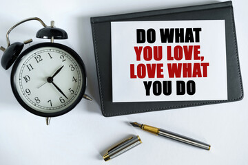 On the table there is a clock, a pen, a notebook and a card on which the text is written - DO WHAT YOU LOVE, LOVE WHAT YOU DO