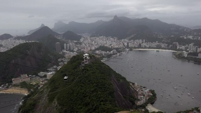 Establishing panoramic view of downtown Rio de Janeiro from rocky mount Sugar Loaf mountain with scenic view of tropical sandy beach and ocean sea on grey cloudy day, South America, handheld pan