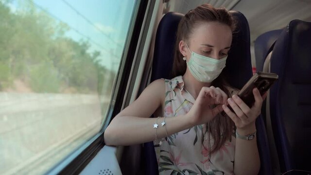 Woman in medical mask driving by train and passing dark tunnel, concentrated female using mobile phone for chatting online and browsing internet. Behavior in public transport during coronavirus