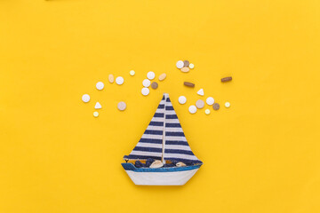Treatment of seasickness. Sailboat and bottle of pills on yellow background. Top view - obrazy, fototapety, plakaty