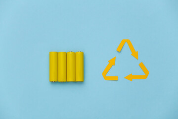 Four yellow AA batteries with recycle symbol on blue pastel background. Top view