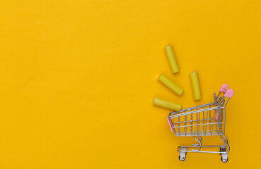 Shopping trolley with Four yellow AA batteries on yellow background. Top view