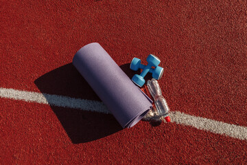 Training equipment on the stadium track. Mat, dumbbells and a bottle of water. Outdoor workout