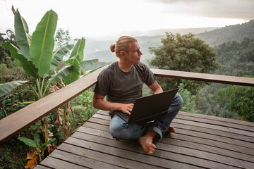 Young man sitting using laptop against scenery landscape forest and mountains, remote work