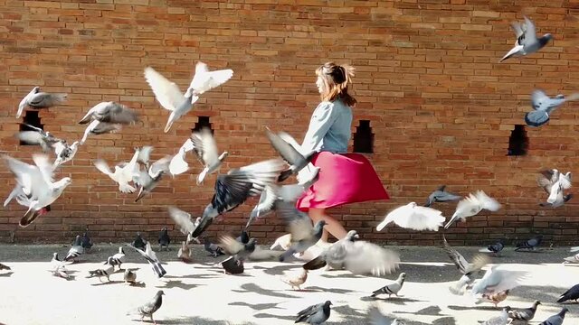 cute Chinese lady with a red dress and denim jacket, turning around herself happily with flying pigeons, and smiling to the camera, at Tha Pae Gate, Chiang Mai, Thailand. Slow-motion shot.