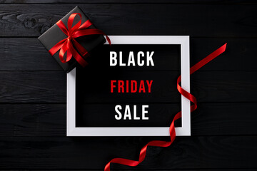 Fototapeta na wymiar Black Friday. Top view of white photo frame with red ribbon on black wooden background with copy space for text.