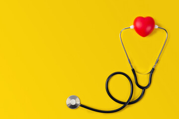 Top view world heart day stethoscope with red heart on yellow background.