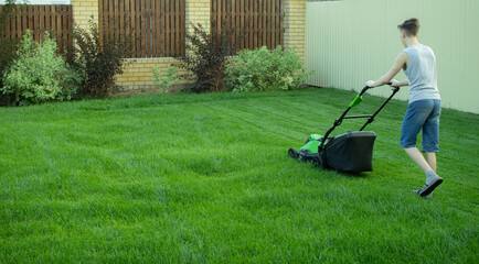 A teenager mows the lawn with a lawn mower.