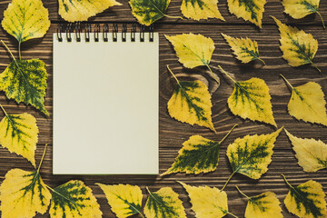Notepad in a frame of yellow leaves on a wooden background. Creative flat lay autumn composition. Top view, copy space. - obrazy, fototapety, plakaty