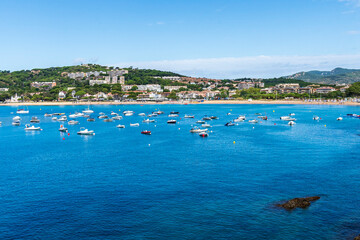 Sant Pol Beach with boats in the sea in a day with some white clouds.