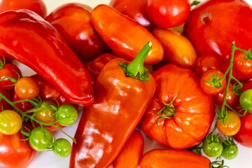 Red peppers, tomatoes, and a green cherry on a white table close up