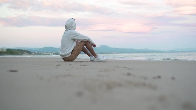 Man seated is starring at the sunrise on the beach at the sea