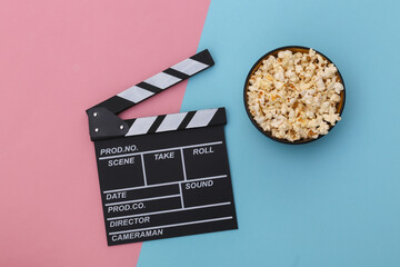 Movie clapper board, popcorn bowl on pink blue background. Entertainment industry. Top view. Flat lay