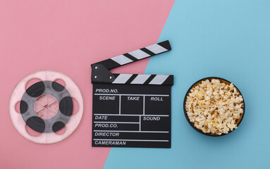 Movie clapper board, popcorn bowl and film reel on pink blue background. Entertainment industry....