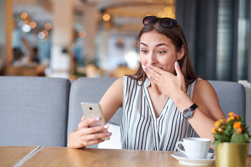 Business woman having surprised expression after recieving message in coffee shop. Wow effect